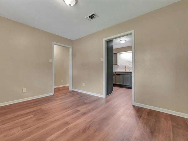 unfurnished room with a sink, baseboards, light wood finished floors, and visible vents