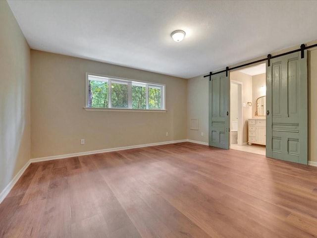 unfurnished bedroom with baseboards, a barn door, and light wood-style flooring