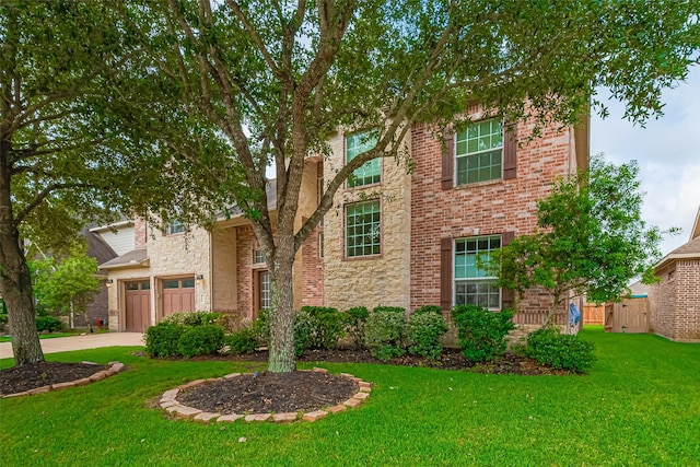 traditional home with a front yard, fence, concrete driveway, an attached garage, and stone siding