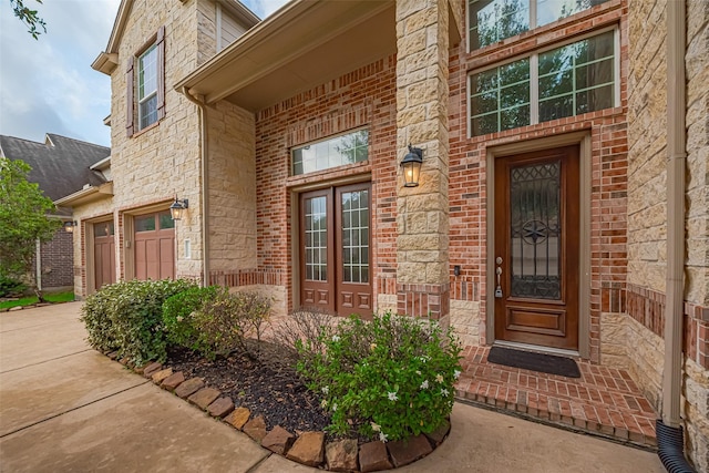 view of exterior entry featuring brick siding, an attached garage, driveway, and stone siding