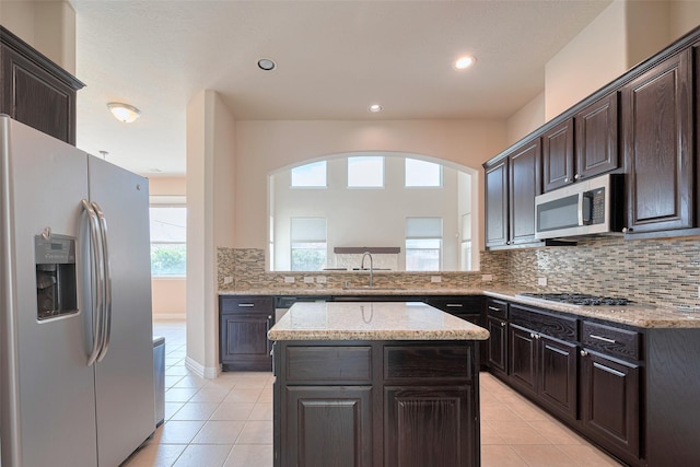 kitchen featuring backsplash, appliances with stainless steel finishes, a kitchen island, and light tile patterned floors