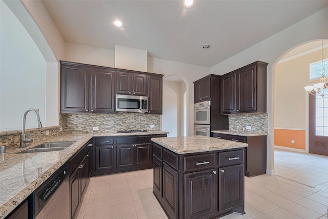 kitchen with a sink, arched walkways, light tile patterned floors, and stainless steel appliances