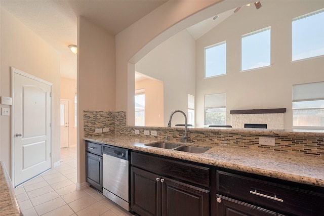 kitchen featuring stainless steel dishwasher, decorative backsplash, arched walkways, a sink, and light tile patterned floors