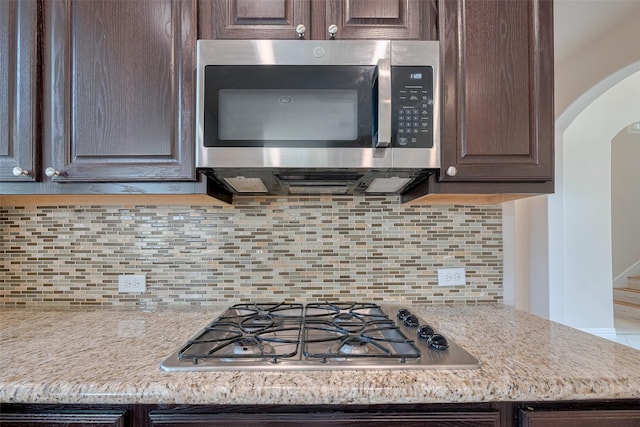 kitchen featuring stainless steel appliances, dark brown cabinetry, arched walkways, and tasteful backsplash
