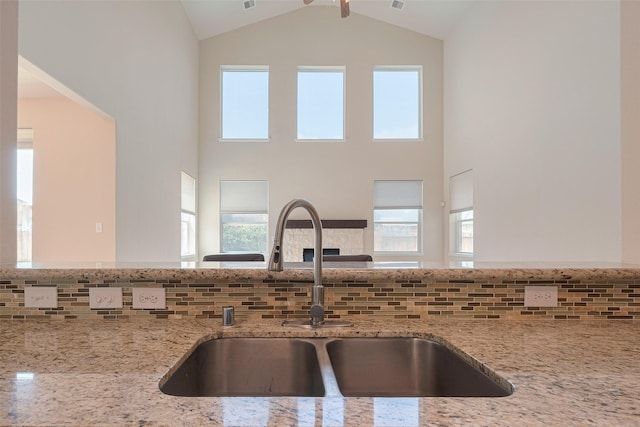 kitchen featuring high vaulted ceiling, light stone counters, a sink, and tasteful backsplash