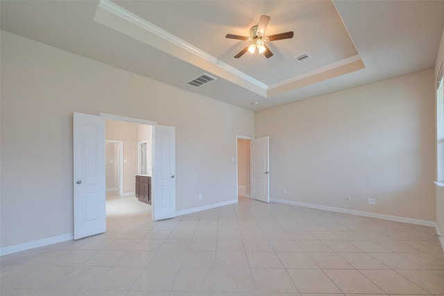 spare room with crown molding, a raised ceiling, a ceiling fan, and visible vents
