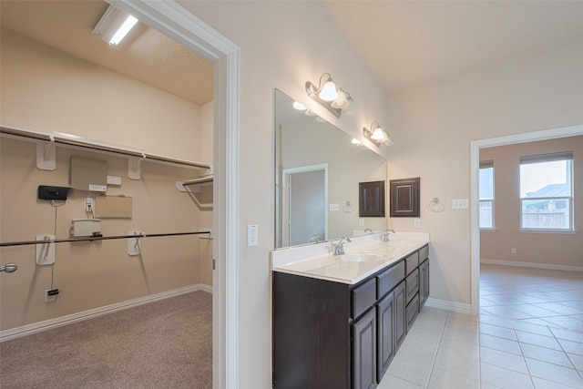 full bath with double vanity, a walk in closet, a sink, tile patterned floors, and baseboards