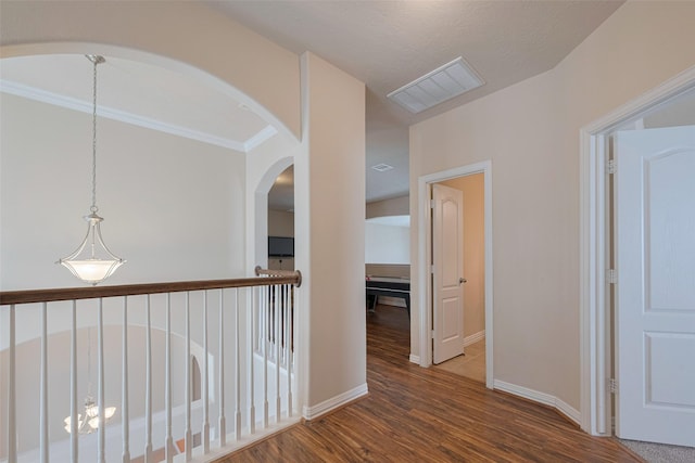 hallway with visible vents, crown molding, arched walkways, wood finished floors, and baseboards