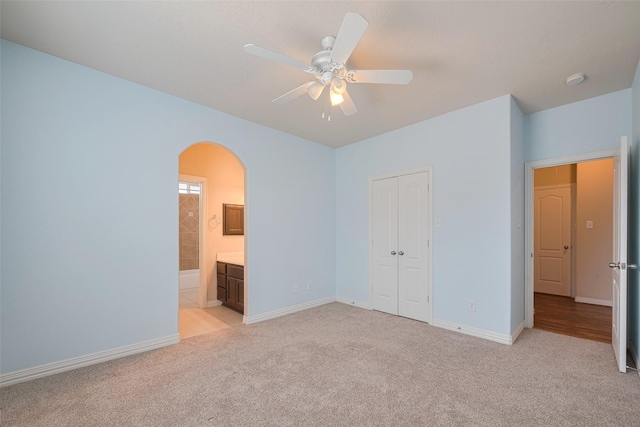 unfurnished bedroom featuring arched walkways, baseboards, light carpet, and a closet