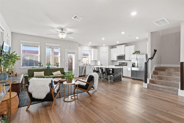 living area with a ceiling fan, visible vents, light wood finished floors, and stairway