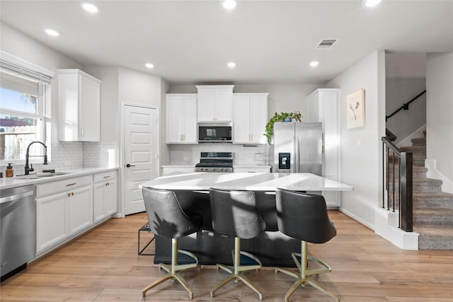 kitchen featuring visible vents, a kitchen island, white cabinets, a sink, and stainless steel appliances