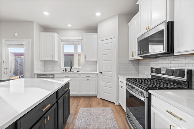kitchen featuring a sink, appliances with stainless steel finishes, white cabinets, and light countertops