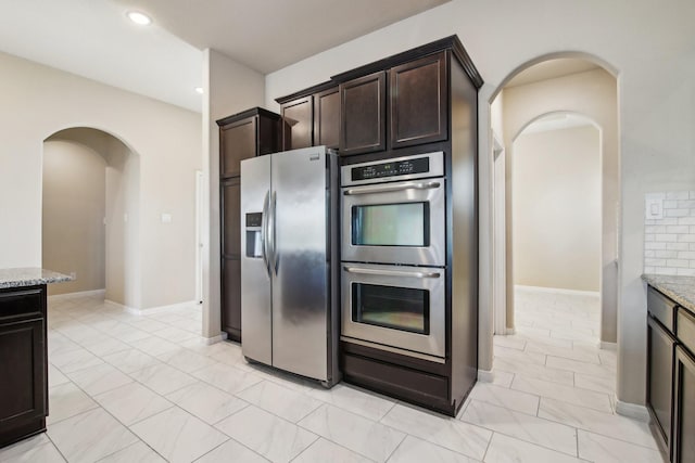4310 Treccia Ct, Katy, TX 77493 - kitchen featuring appliances with stainless steel finishes, arched walkways, light stone counters, dark brown cabinets, and recessed lighting