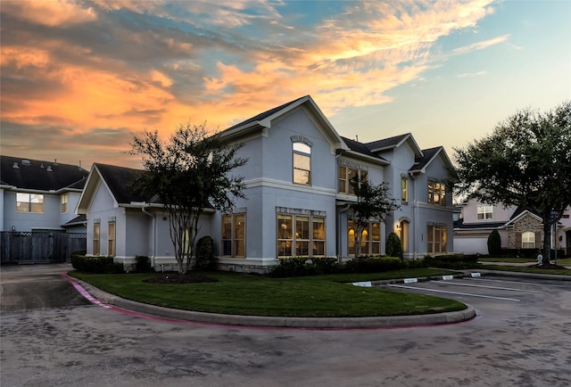 view of front of house featuring a lawn, fence, stucco siding, and uncovered parking