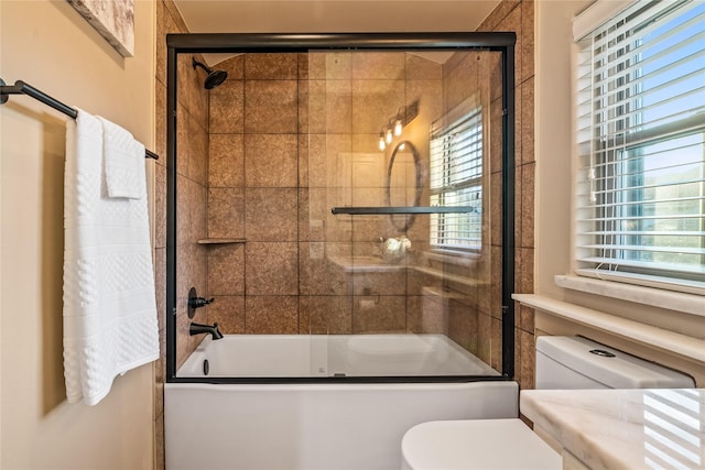 bathroom with combined bath / shower with glass door, a healthy amount of sunlight, and toilet