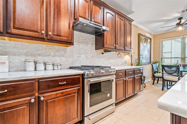 kitchen with light countertops, stainless steel range with gas cooktop, a ceiling fan, light tile patterned floors, and under cabinet range hood