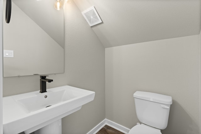 half bathroom featuring toilet, a sink, visible vents, baseboards, and lofted ceiling
