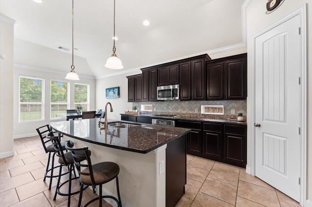 kitchen with a sink, stainless steel microwave, light tile patterned floors, backsplash, and vaulted ceiling