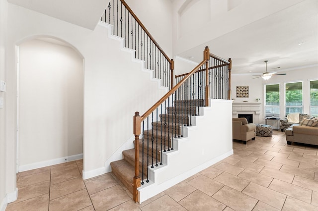 stairway with ceiling fan, arched walkways, a fireplace, baseboards, and tile patterned floors