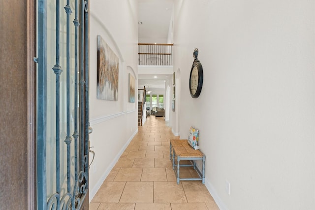 hallway featuring light tile patterned floors, baseboards, and a high ceiling