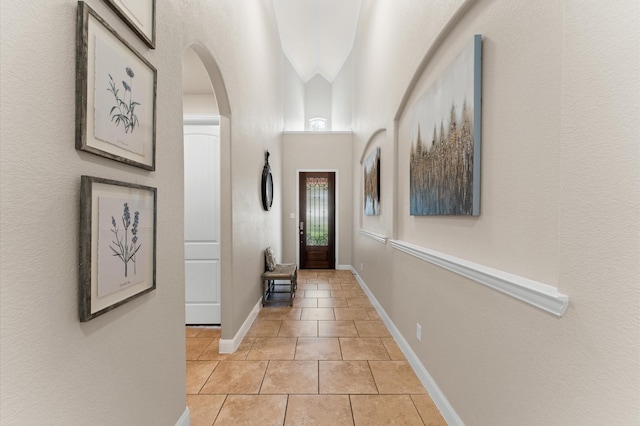 hallway featuring baseboards, arched walkways, and light tile patterned floors