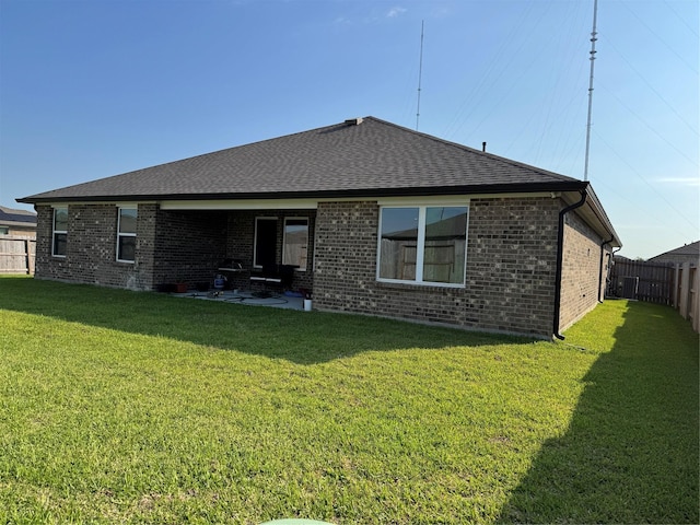 back of house with a yard, brick siding, roof with shingles, and a fenced backyard