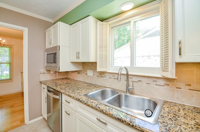 kitchen with appliances with stainless steel finishes, a sink, crown molding, healthy amount of natural light, and white cabinetry
