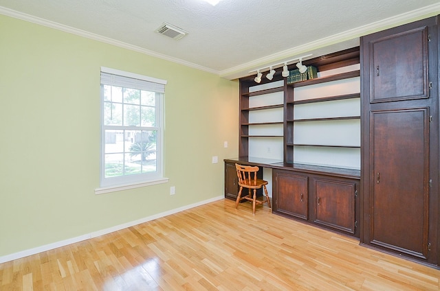 unfurnished office with light wood finished floors, crown molding, baseboards, a textured ceiling, and built in desk