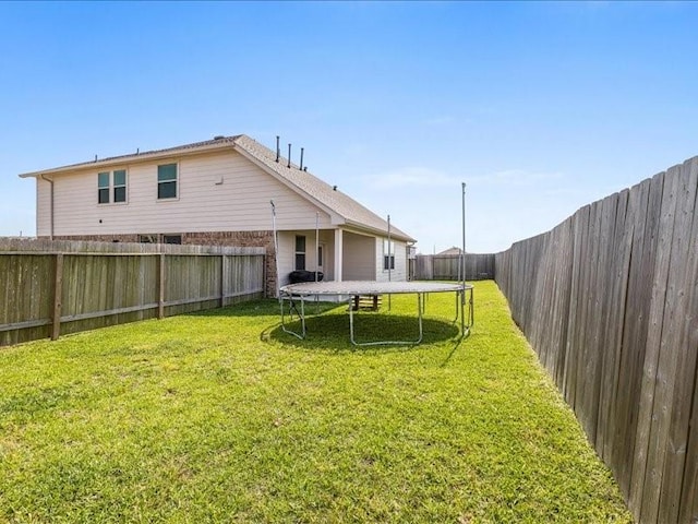 rear view of property with a fenced backyard, a trampoline, and a yard