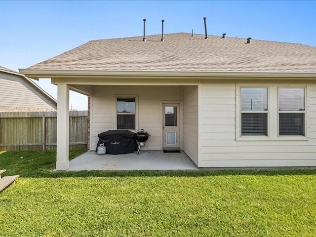 rear view of property featuring fence, a shingled roof, a lawn, and a patio area