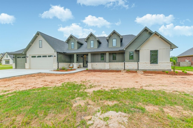 view of front facade with covered porch, stone siding, roof with shingles, an attached garage, and driveway