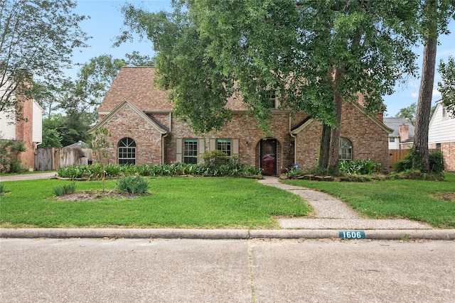 tudor home featuring fence, a front yard, roof with shingles, and brick siding