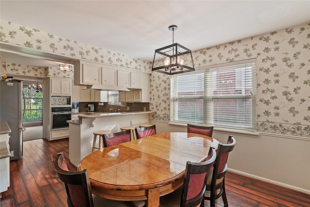 dining area featuring an inviting chandelier, a wainscoted wall, dark wood-style flooring, and wallpapered walls