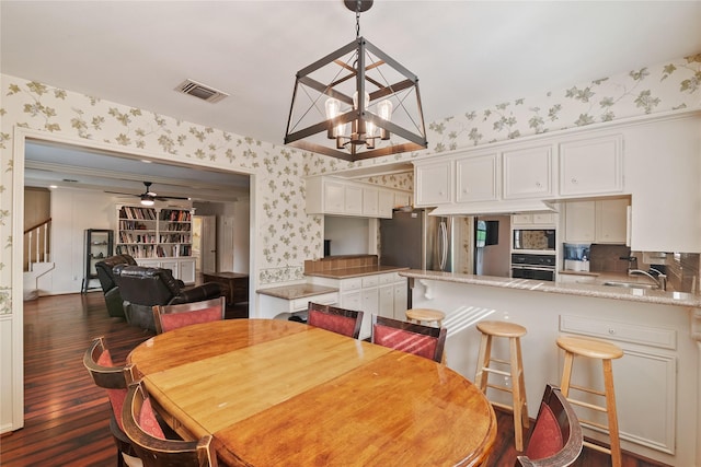 dining area featuring dark wood-style flooring, ceiling fan with notable chandelier, wallpapered walls, visible vents, and stairway