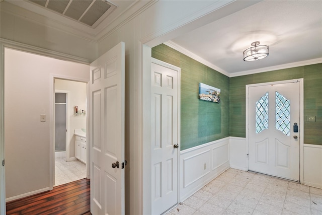 foyer with crown molding, wainscoting, a decorative wall, light floors, and visible vents