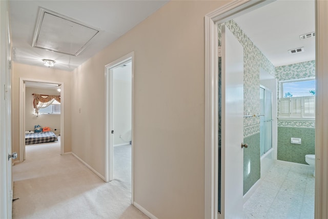 hallway featuring visible vents, attic access, baseboards, and carpet
