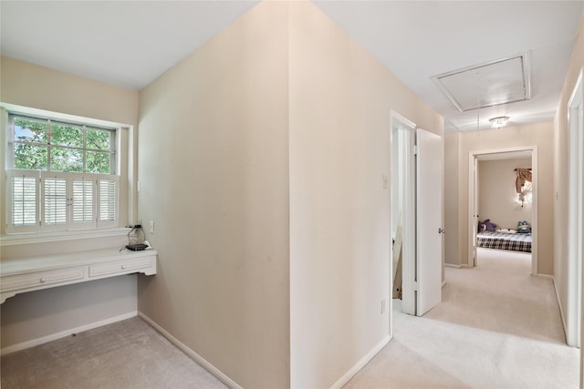 hallway with baseboards, attic access, and light colored carpet