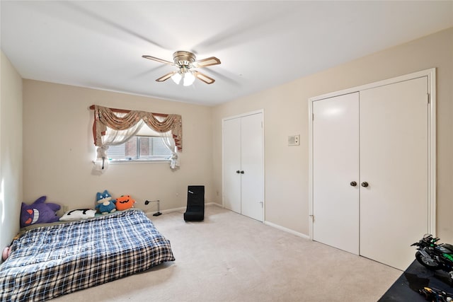bedroom featuring light colored carpet, a ceiling fan, baseboards, and two closets