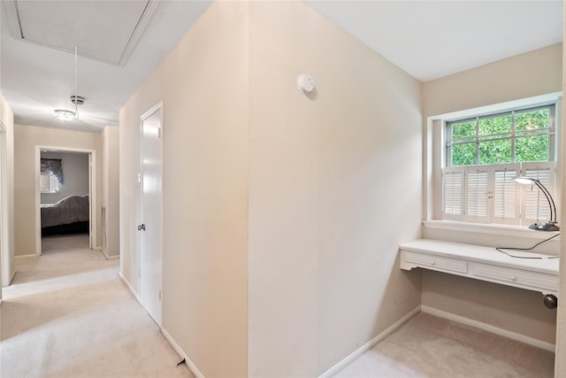 corridor with baseboards, light carpet, and attic access