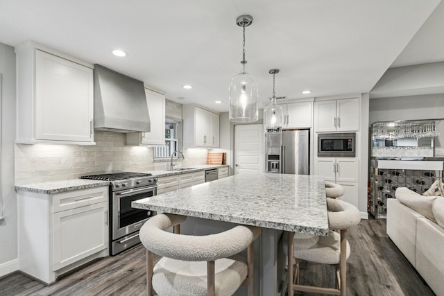 kitchen with a breakfast bar area, dark wood-style floors, wall chimney exhaust hood, a sink, and stainless steel appliances