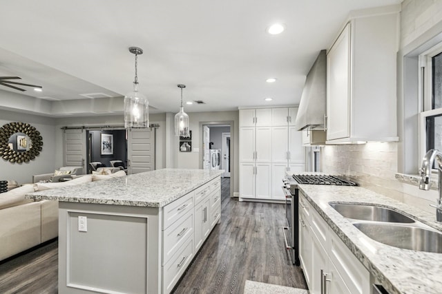 kitchen with high end stainless steel range, a sink, wall chimney exhaust hood, recessed lighting, and open floor plan