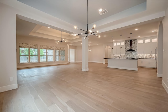 unfurnished living room featuring baseboards, visible vents, a tray ceiling, and a notable chandelier