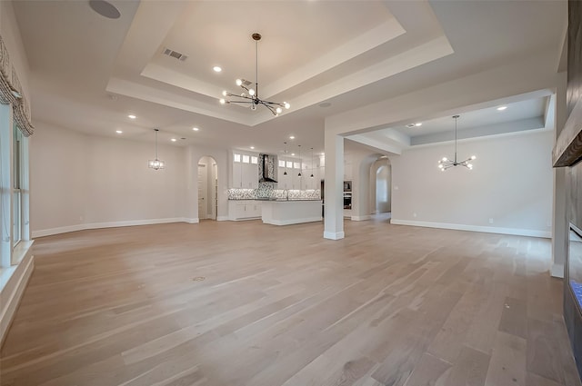 unfurnished living room with an inviting chandelier, arched walkways, recessed lighting, a tray ceiling, and visible vents