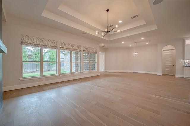 spare room featuring baseboards, light wood-type flooring, a chandelier, a tray ceiling, and arched walkways