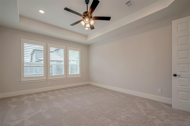 spare room with light colored carpet, a ceiling fan, baseboards, and a tray ceiling
