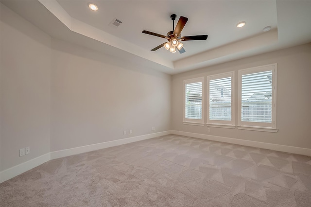 unfurnished room featuring ceiling fan, visible vents, light colored carpet, baseboards, and a tray ceiling