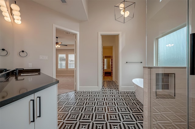 full bathroom featuring a sink, double vanity, a ceiling fan, baseboards, and a soaking tub