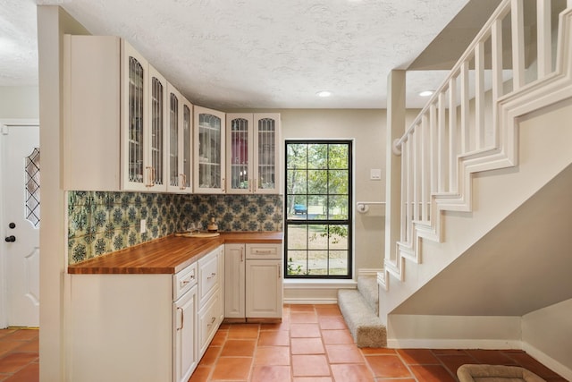 302 Tall Pines Dr, Magnolia, TX 77354 - kitchen with butcher block countertops, decorative backsplash, a textured ceiling, and glass insert cabinets