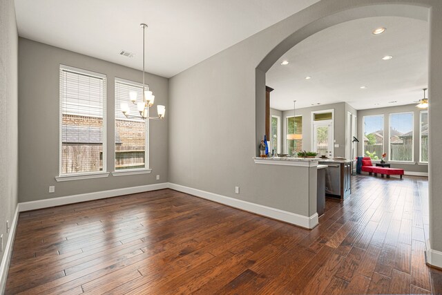empty room featuring arched walkways, baseboards, dark wood finished floors, recessed lighting, and a chandelier