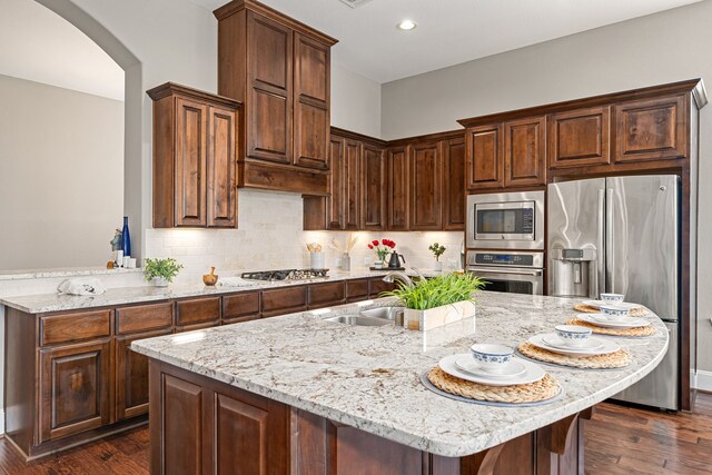 kitchen with stainless steel appliances, arched walkways, light stone countertops, dark wood-style flooring, and recessed lighting